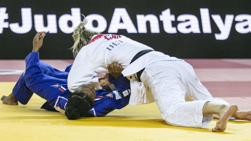 Deux judokas se battent sur un tatami, une concurrente a retourné l'autre qui est couchée par terre.  