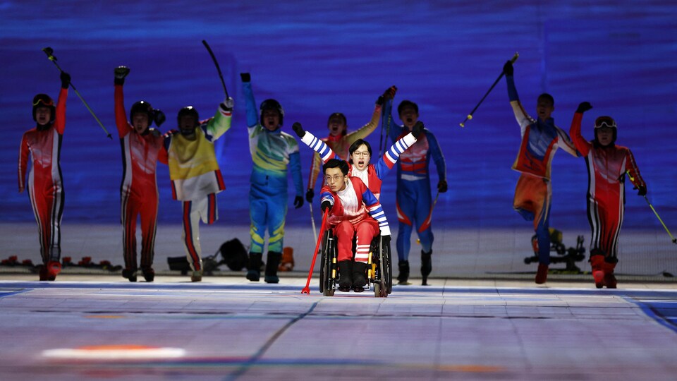 Sous les encouragements d'autres sportifs, un joueur de curling en fauteuil roulant chinois projette une pierre.