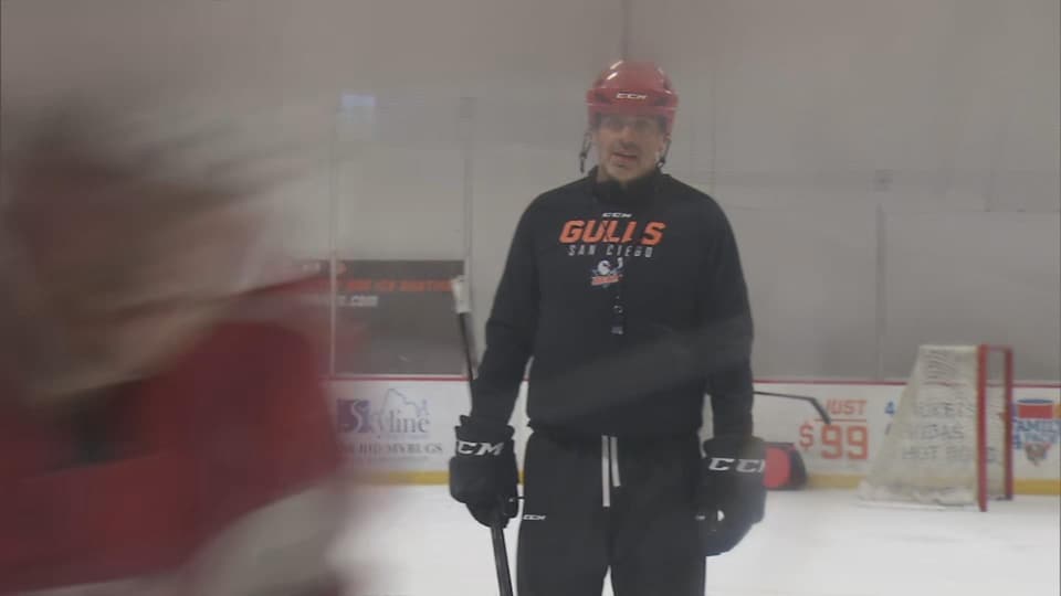 L'entraîneur des Gulls, casqué et en vêtements d'entraînement, dirige ses joueurs sur la glace.