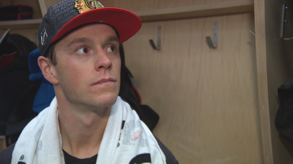 Jonathan Toews, assis dans le vestiaire, avec une casquette de son équipe, une serviette autour du cou, l'air pensif.