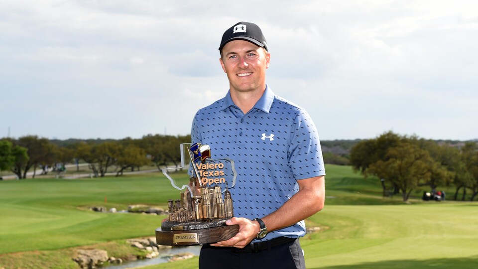 Un joueur de golf sur un terrain tient un trophée dans ses mains.