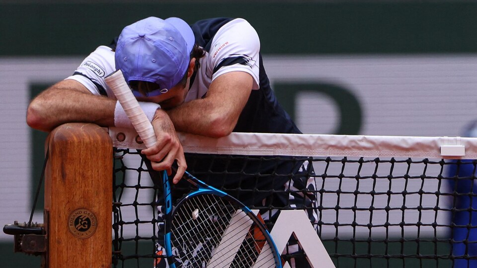 A tennis player bent down and laid his head and arms on the net in despair. 