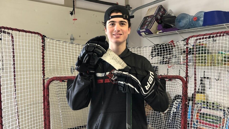 Jeune homme avec casquette, tenant son bâton de hockey.