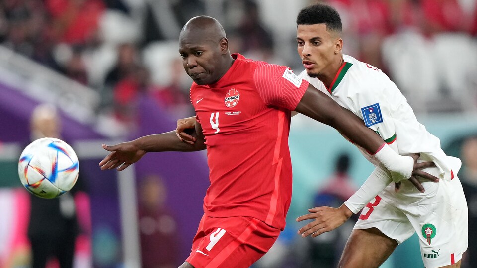 Le défenseur de l'équipe canadienne tente d'empêcher le joueur marocain d'atteindre le ballon en se plaçant devant lui