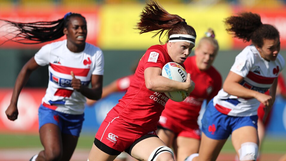 Elle court avec un ballon de rugby dans sa main droite.