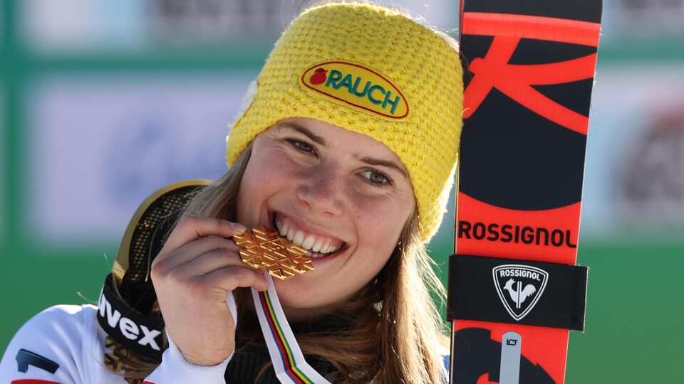 Une skieuse croque une médaille d'or en forme de flocon.