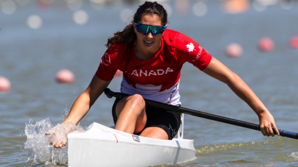 Une femme portant les couleurs du Canada est dans une petite embarcation blanche, sur l'eau.