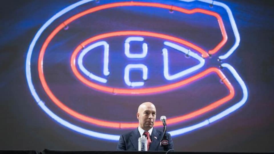 A man in front of a black background with a neon team logo