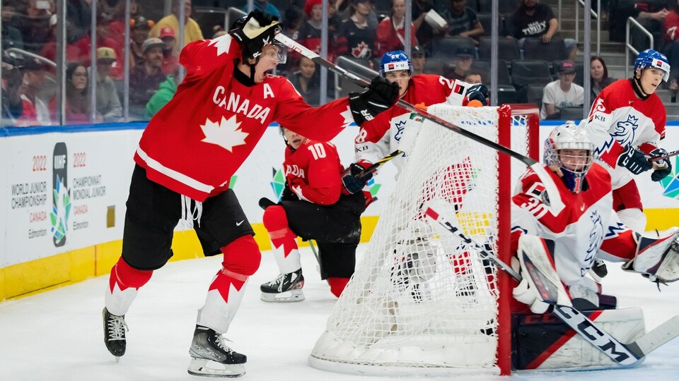 Installé derrière le filet, un hockeyeur porte la rondelle dans le but.