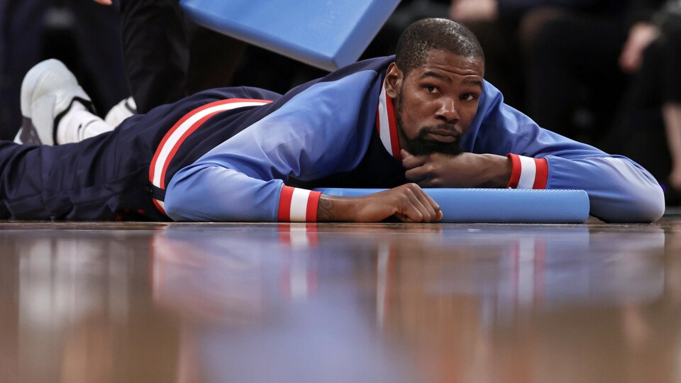 Kevin Durant est allongé sur un terrain de basketball. Un thérapeute lui masse les cuisses.