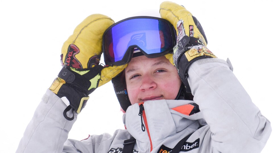 La skieuse a les mains gantées sur ses lunettes et sourit pour la photo.