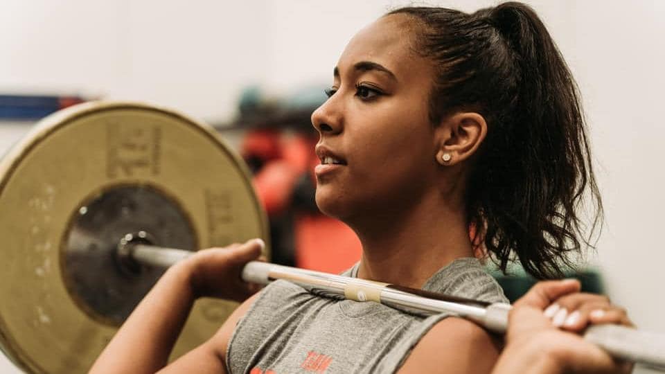 Elle tient une barre sur ses épaules à l'entraînement.