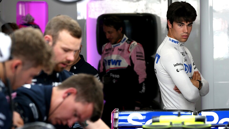 Lance Stroll regarde sa monoplace dans le garage de Racing Point pendant que les mécaniciens travaillent.