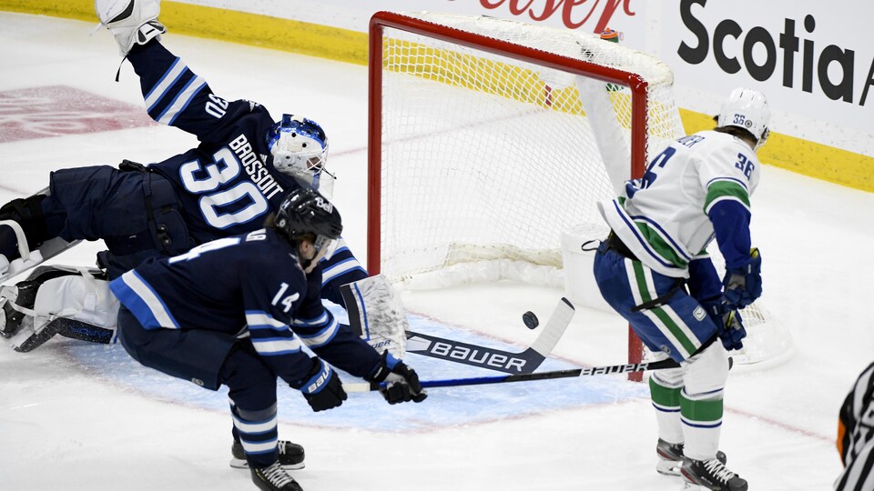 L'attaquant des Canucks Nils Hoglander regarde son tir rentrer dans le filet des Jets, alors que le gardien Laurent Brossoit plonge, en vain, pour tenter un arrêt.