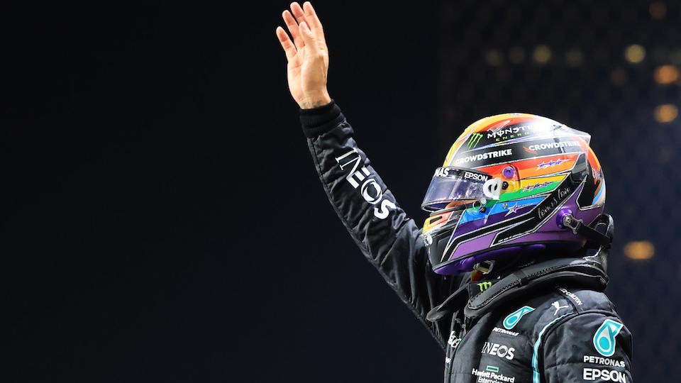A helmeted pilot waves to the crowd with his right hand. 
