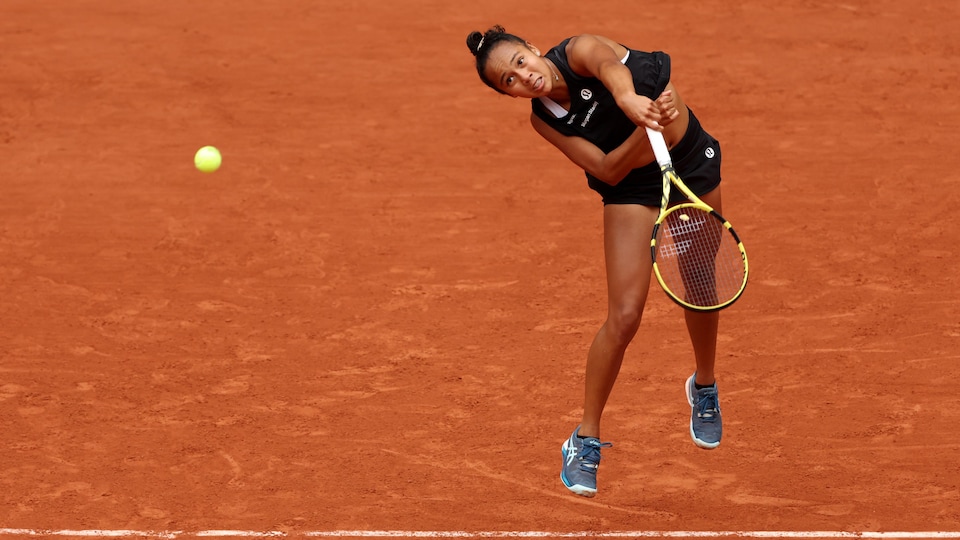 Une joueuse de tennis vêtue de noir regarde la balle qu'elle vient de frapper en service au tournoi de Roland-Garros. 