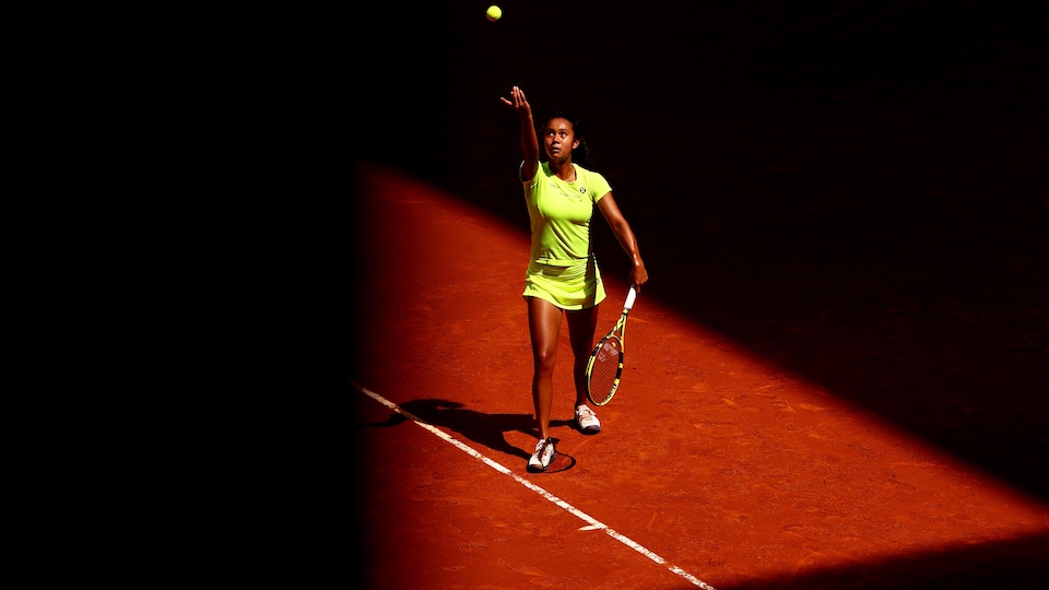 A tennis player throws the ball in the air while serving on a clay court. 