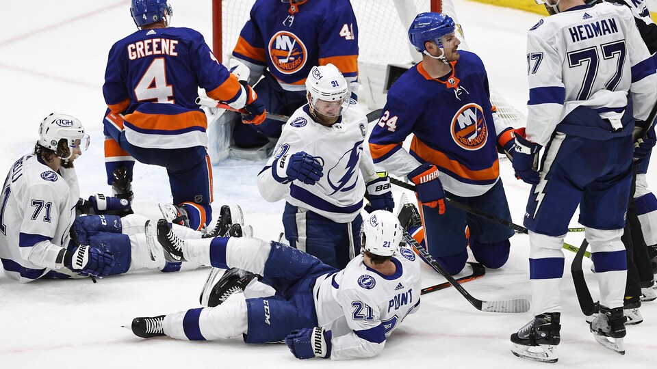 Brayden Point, assis sur la glace, est félicité par Steven Stamkos après avoir marqué un but, pendant que deux joueurs des Islanders se relèvent, dépités.