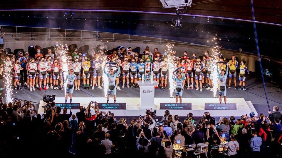 Quatre cyclistes lèvent leurs trophées devant leurs adversaires et la foule. 