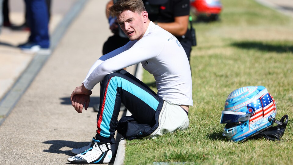 Un pilote de course est assis dans l'herbe et regarde à sa gauche.