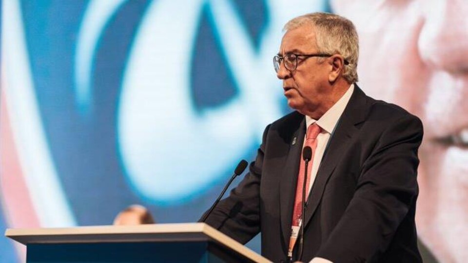 Un homme derrière un lutrin prononce un discours.
