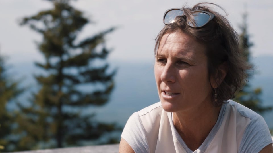 Une femme de profil, lunettes sur la tête, au sommet d'une montagne