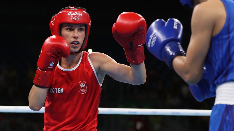La boxeuse, vêtue de rouge, est en plein combat.