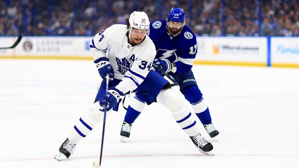 Two hockey players skated behind the puck.