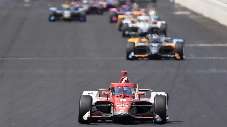 An IndyCar-style race car, shot directly, was a few steps ahead of the peloton.