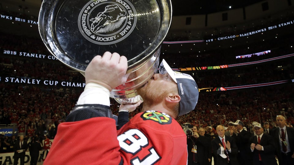 A man kisses the Stanley Cup he holds in his arms.