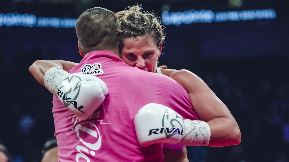 Une boxeuse et son entraîneur se serrent dans leurs bras sur le ring.