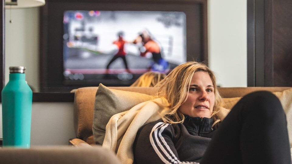 Une femme couchée sur un fauteuil regarde une télévision.