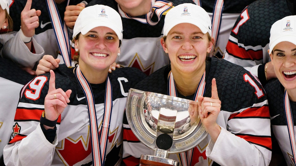 Deux joueuses de hockey de l'équipe canadienne prennent la pose avec leur médaille d'or et un trophée. 