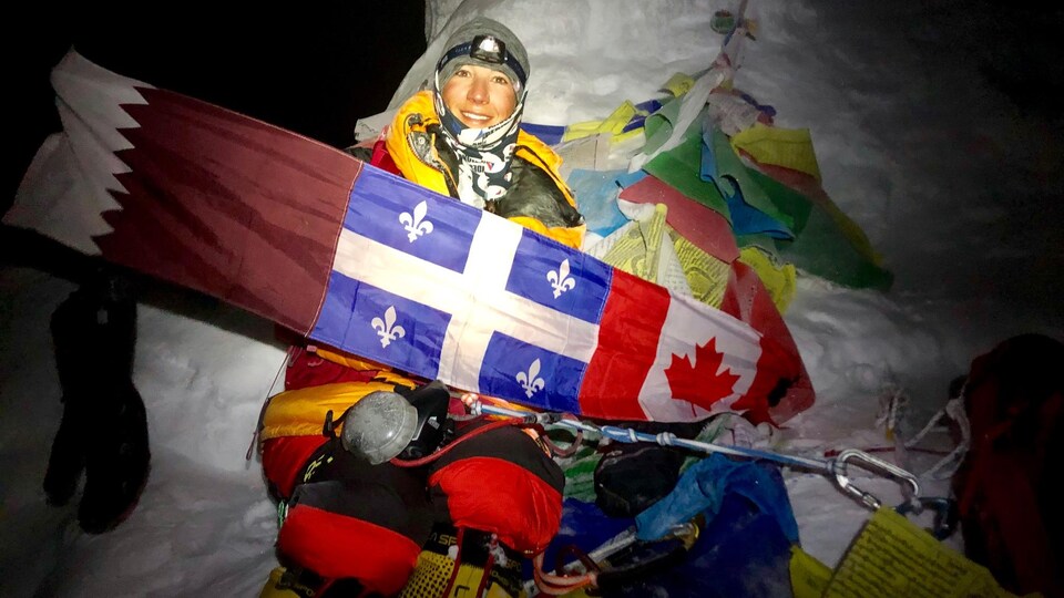 Un escalador muestra las banderas de Qatar, Quebec y Canadá en la oscuridad en la cima de una montaña en Nepal. 