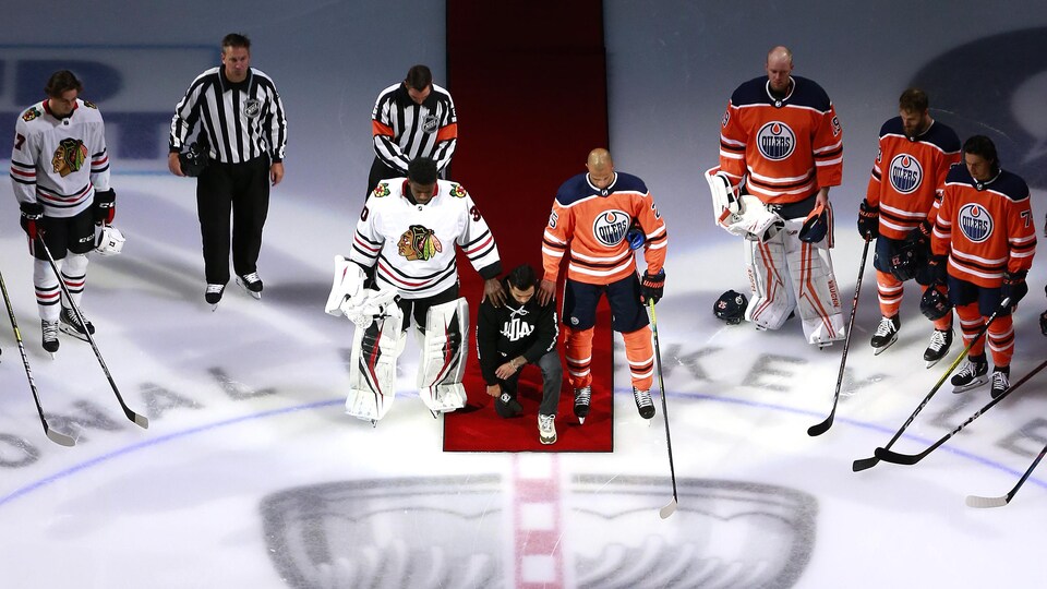 Matthew Dumba, de l'Alliance pour la diversité au hockey (HDA) et joueur du Wild du Minnesota, s'agenouille pendant l'hymne américain avant le match entre les Blackhawks et les Oilers. Malcolm Subban, des Blackhawks, et Darnell Nurse, des Oilers, posent une main sur ses épaules.