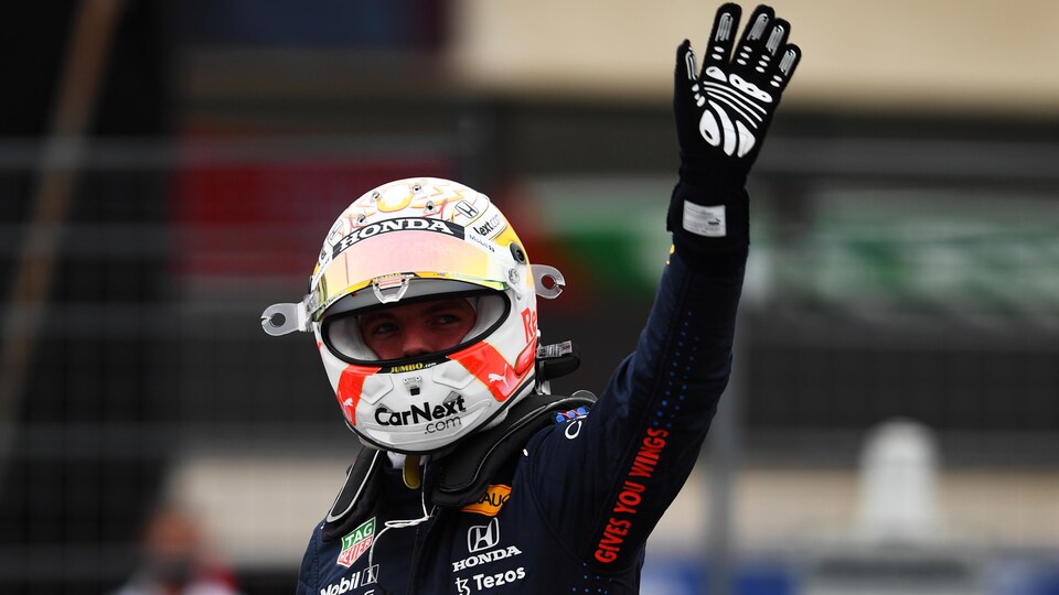 Max Verstappen, casqué, lève le bras gauche.