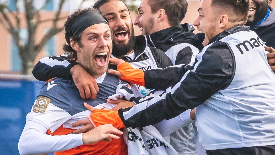 Un joueur de soccer est entouré de ses coéquipiers après avoir marqué un but.