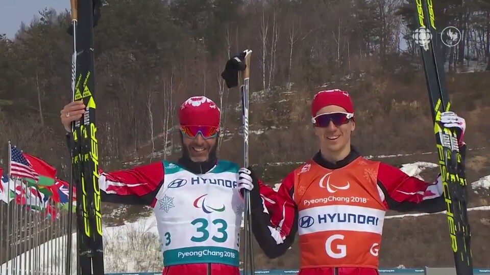 Deux fondeurs lèvent leurs skis et saluent pour la photo.