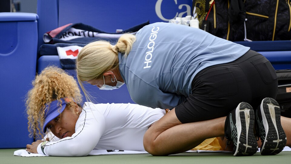 Une joueuse de tennis est couchée au sol pendant qu'une thérapeute l'examine.