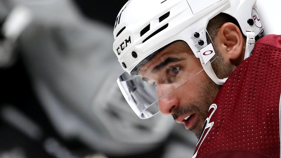 Gros plan du visage d'un joueur de hockey, de profil, pendant un match, il attend la mise au jeu. Il a un casque avec protecteur facial.