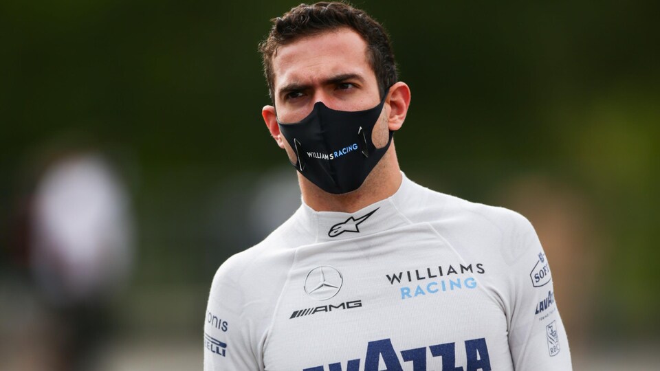 Un pilote en combinaison de course, sans son casque, et avec un masque