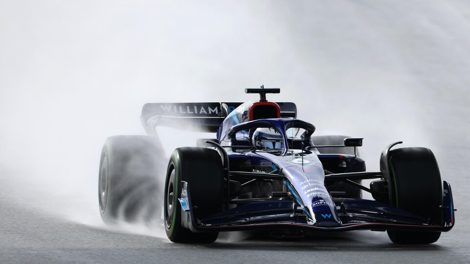 Un pilote de F1 tourne sur un circuit détrempé, des gerbes d'eau s'échappent des pneus. 