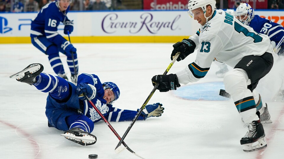 Un défenseur des Maple Leafs tombe sur la glace en tentant de repousser un joueur des Sharks qui contrôle le disque devant le filet.