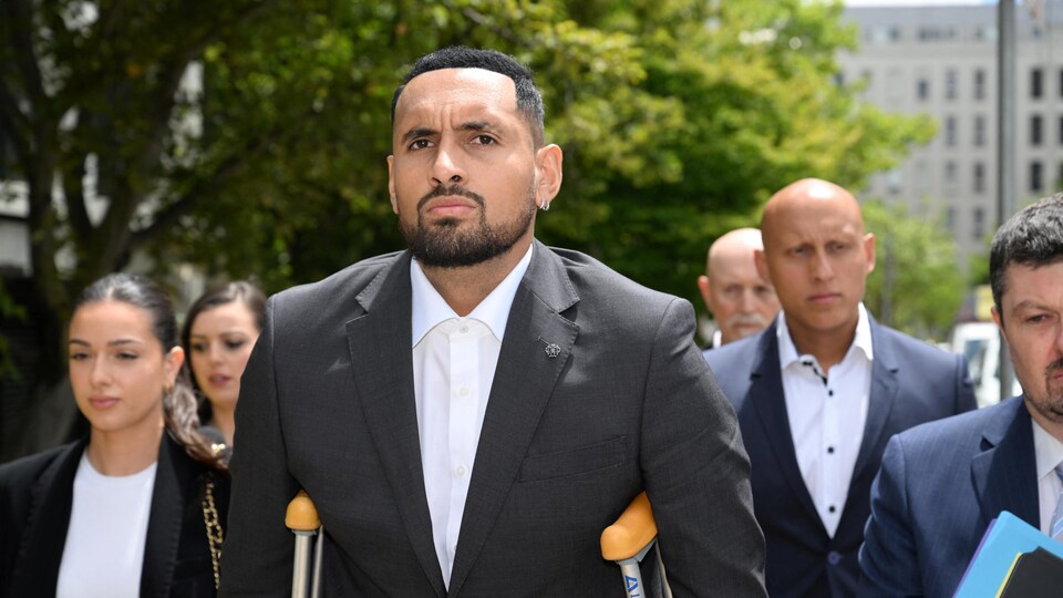 L'homme vêtu d'un veston noir et d'une chemise blanche arrive au palais de justice en béquilles.