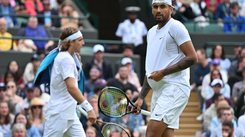 Deux joueurs de tennis, habillés de blanc, changent de côté sur un terrain gazonné pendant un match.