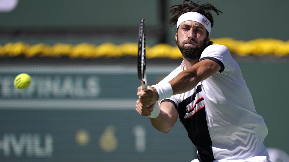 Le joueur de tennis frappe la balle, les deux mains sur sa raquette.