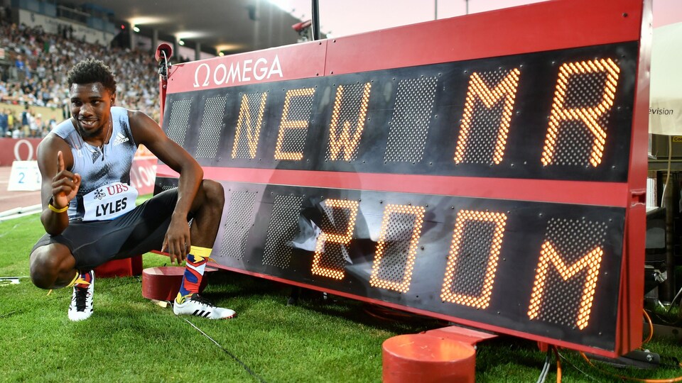 Il est tout sourire à côté du panneau montrant qu'il a réussi un record de compétition au 200 m.