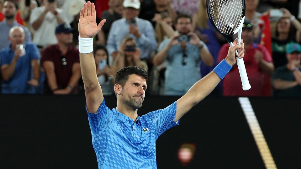 Un joueur de tennis lève les bras, sa raquette dans la main gauche, pour remercier la foule qui l'applaudit. 