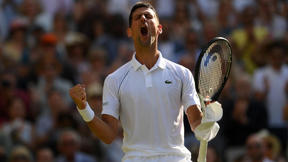 Un joueur de tennis, vêtu de blanc, raquette et casquette dans la main gauche, crie sa joie après une victoire à Wimbledon. 