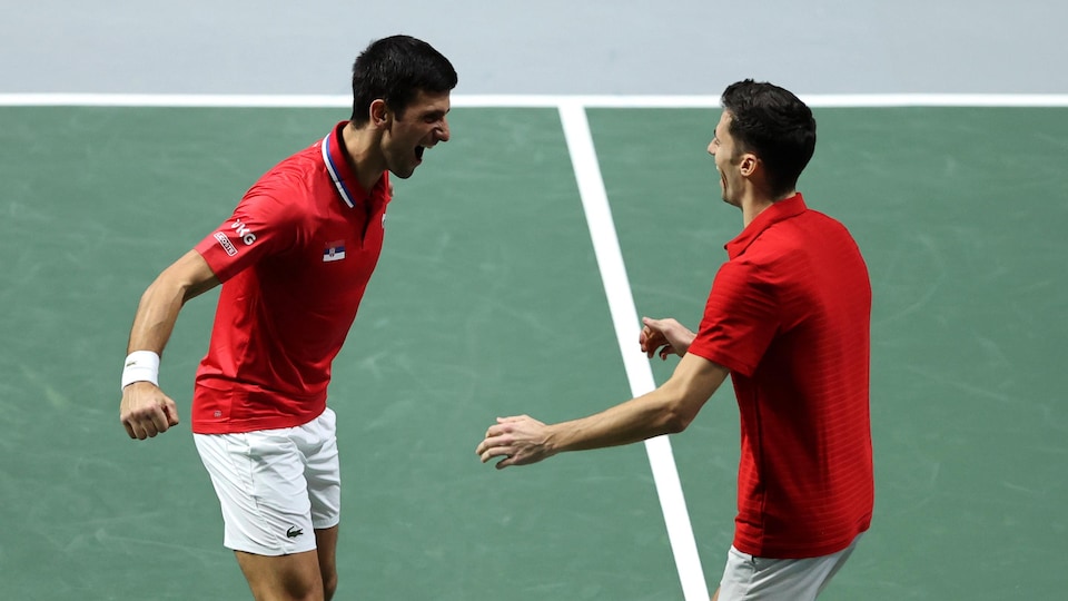 Deux joueurs de tennis habillés en blanc et rouge se regardent, très heureux.